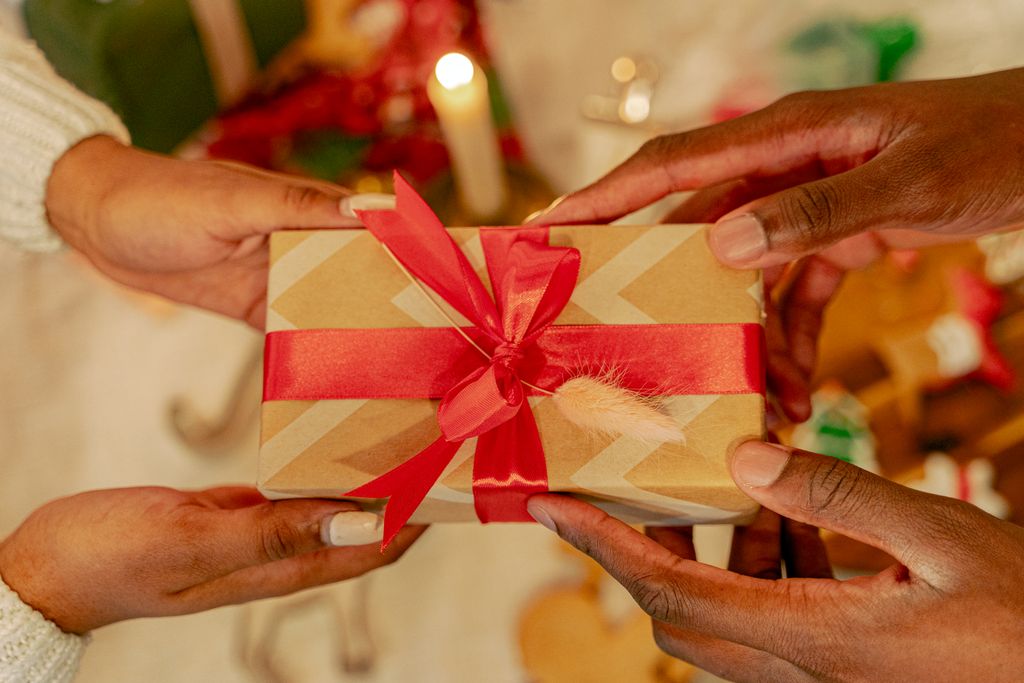 Two hands exchanging a wrapped gift with red ribbon during festive holiday season.